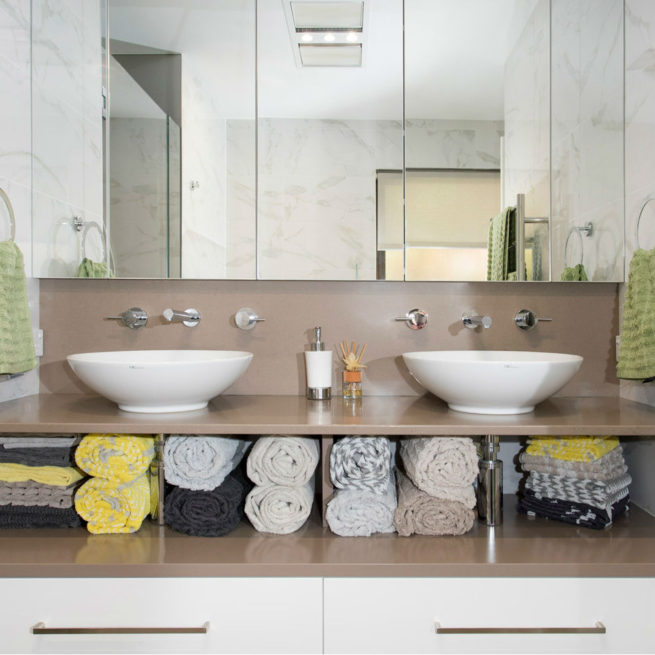 A large mirror above twin basins, beneath which are rolled up towels and closed drawers